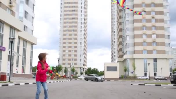 Девушка запускает воздушного змея на ветру среди зданий — стоковое видео