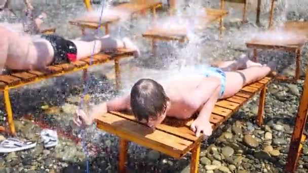 Garçon se trouve sur la chaise longue sous l'eau courante — Video