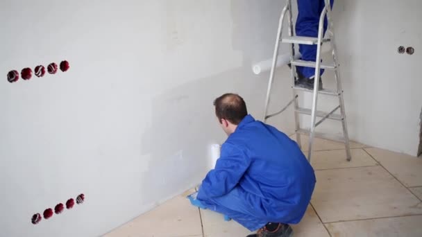 El hombre unta el pegamento a la pared, cerca del hombre sobre la escalera pega la fibra de vidrio — Vídeos de Stock