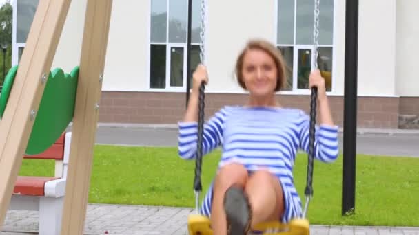 Mladá dívka oblečená v šatech jezdí na houpačce — Stock video
