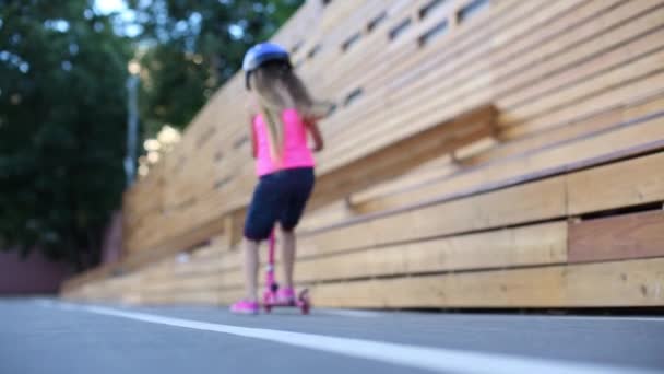 Маленькая девочка в шлеме ездит на скутере — стоковое видео