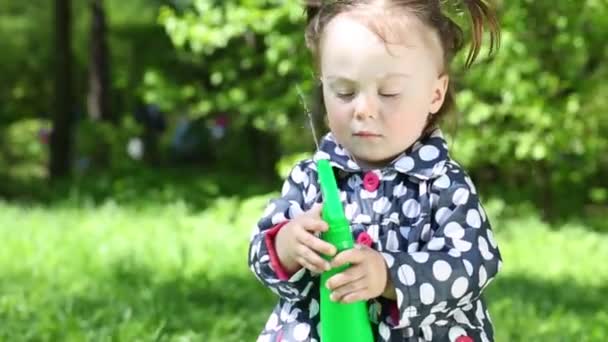 Little girl in raincoat plays with sprayer in summer park — Stock Video