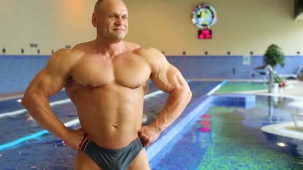 Bodybuilder står nära inomhuspool — Stockvideo