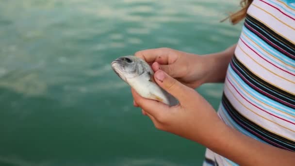 Девушка держит маленькую рыбу на берегу моря — стоковое видео