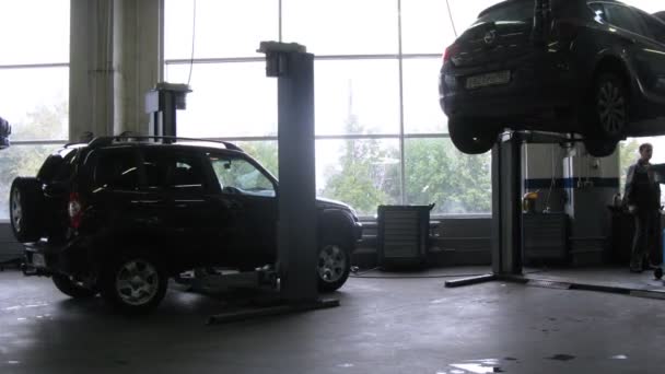 Механики поднимают машины в гараже — стоковое видео
