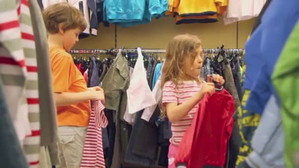 Двое детей смотрят одежду в магазине — стоковое видео