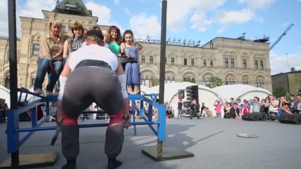 Человек поднимает тяжелую скамейку с людьми — стоковое видео