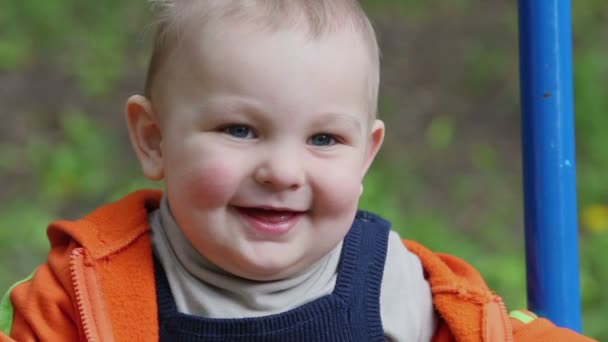 Kleine jongen in oranje jas op schommel — Stockvideo