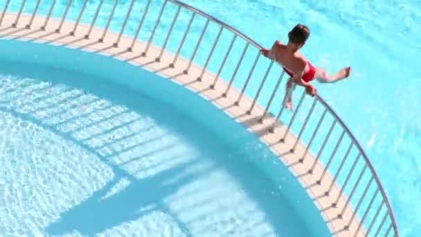 Pojken sitter på ledstången på pool — Stockvideo