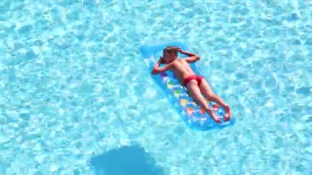 Хлопчик плаває на надувному матраці в басейні — стокове відео