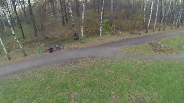 Menino com bicicleta senta-se no banco — Vídeo de Stock