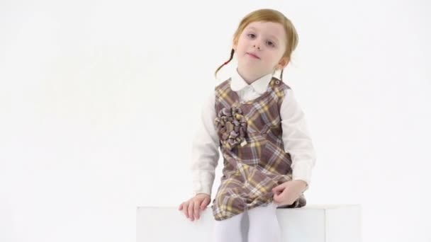 Kleines Mädchen sitzt auf weißem Würfel — Stockvideo