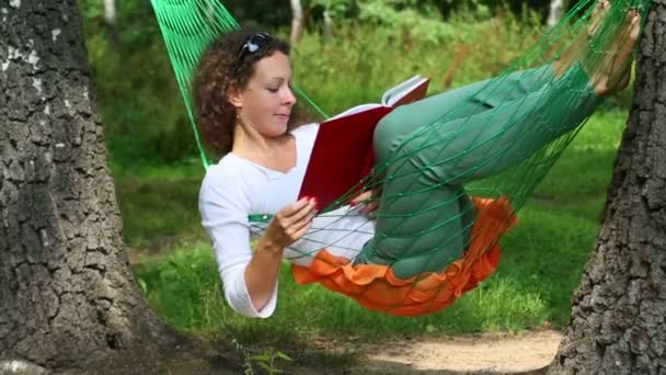Молодая девушка в гамаке и читает книги — стоковое видео