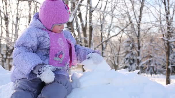 Menina senta-se no snowdrift e joga — Vídeo de Stock