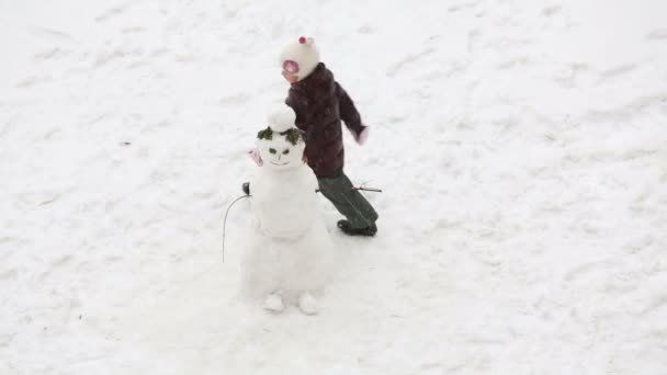 Little girl runs around snowman — Stock Video