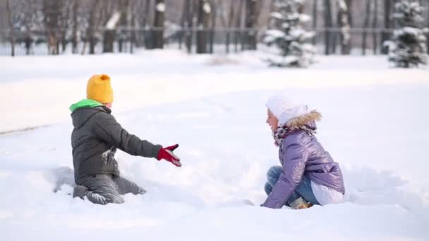 Niño y niña se sientan en la deriva de nieve — Vídeos de Stock