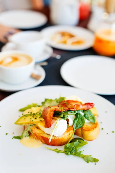 本尼迪克特带鳄梨和熏肉的美味鸡蛋早餐在餐馆里享用 — 图库照片