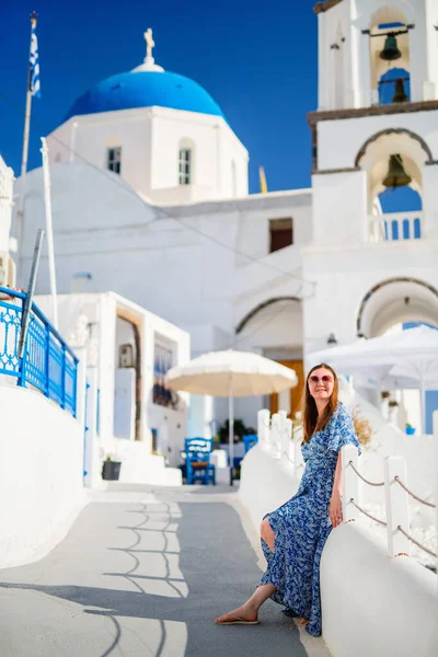 ギリシャのサントリーニ島のピルゴス村を青いドーム型の教会と伝統的な白塗りの家で歩くのを楽しむ美しい若い女性 — ストック写真