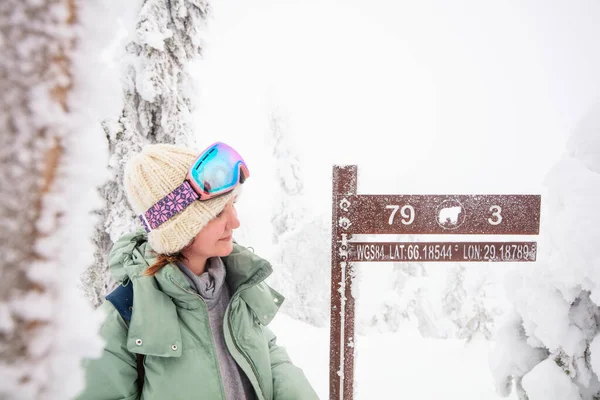 フィンランドのラップランドの雪に覆われた森の中で Valtavaara冬のハイキングコースの標識の横にある若い美しい女性 — ストック写真