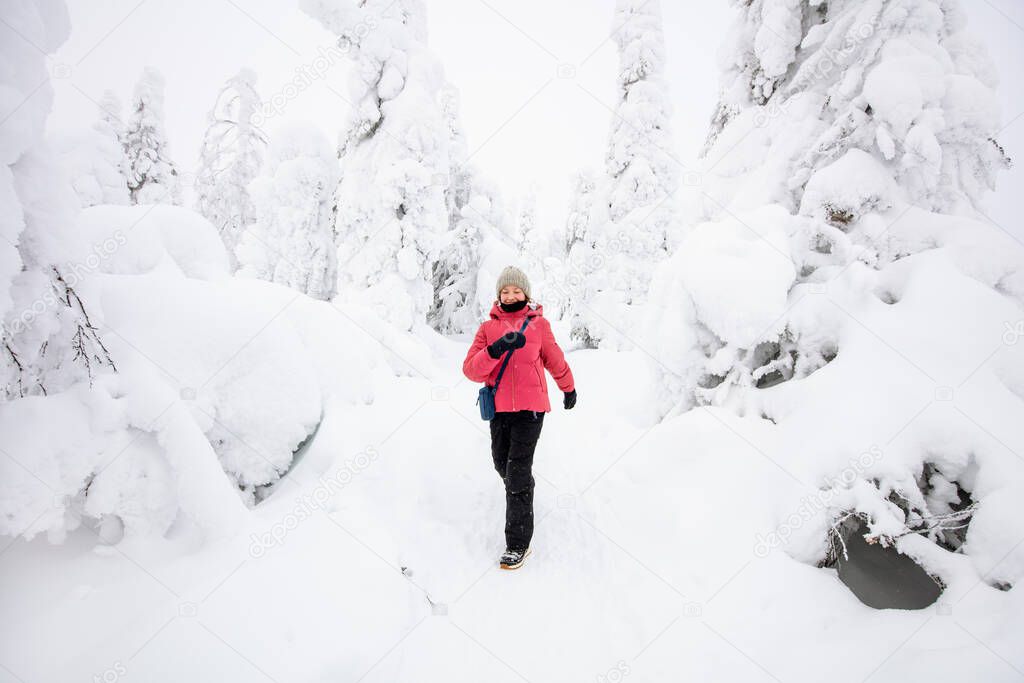 Cute pre-teen girl walking in winter forest among snow covered trees in Lapland Finland