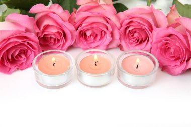 Beyaz arka planda pembe gül ve yanan mumlar