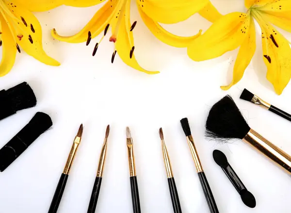 makeup brushes and yellow lily on white background