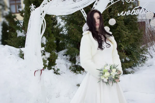 Mooie bruid in een vacht cape met een boeket — Stockfoto