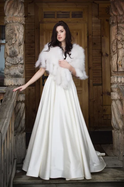 De bruid in een vacht cape op een veranda van een houten huis — Stockfoto