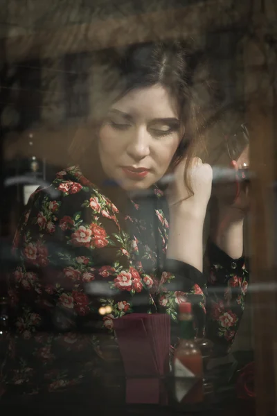 Beautiful woman sits in a cafe, holding a cup, photos behind gla — Stock Photo, Image