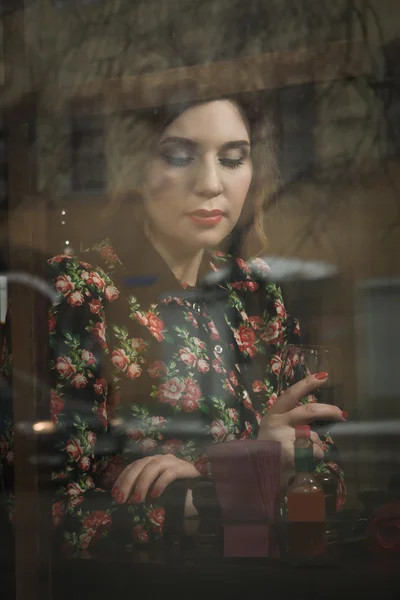 Mulher bonita senta-se em um café, segurando uma xícara, fotos atrás gla — Fotografia de Stock