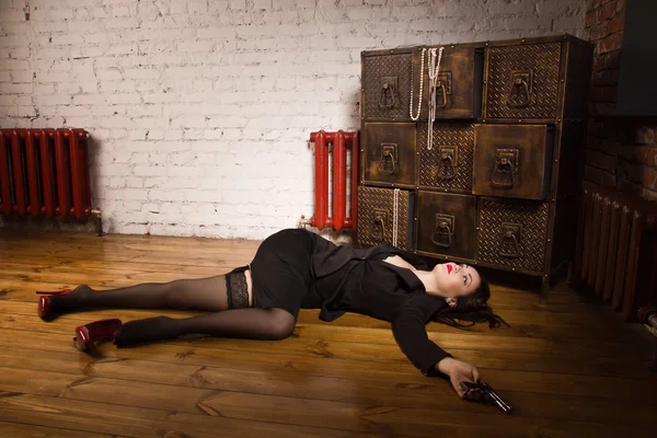 Žena v černém obleku s pistolí, ležící na podlaze — Stock fotografie