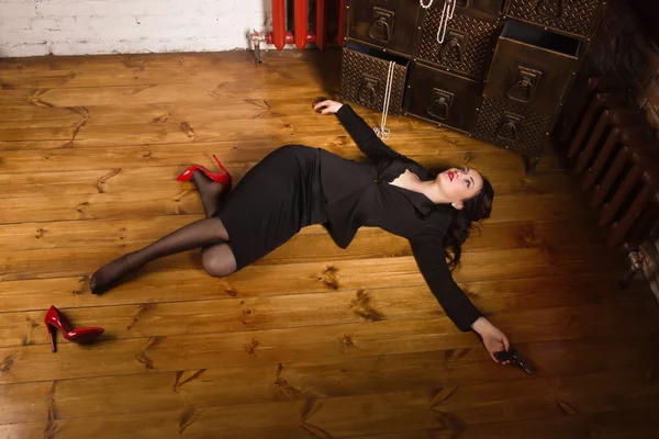 Woman in a black suit with gun lying on the floor — Stock Photo, Image