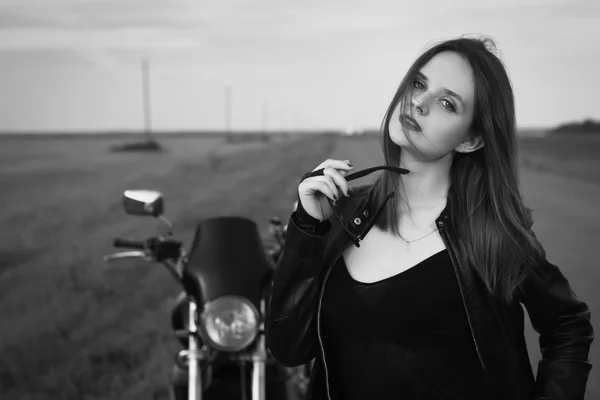 Chica motorista en una chaqueta de cuero posando cerca de la motocicleta — Foto de Stock