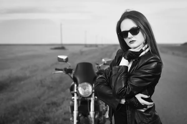 Chica motorista en una chaqueta de cuero posando cerca de la motocicleta — Foto de Stock