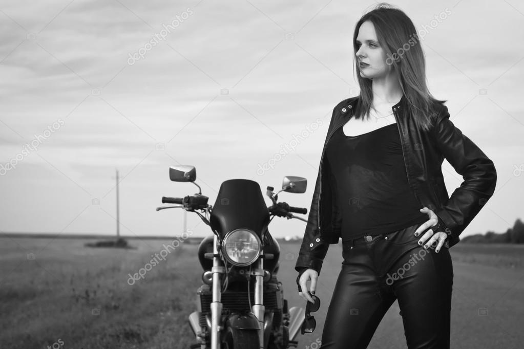 Biker girl in a leather jacket posing near motorcycle Stock Photo by