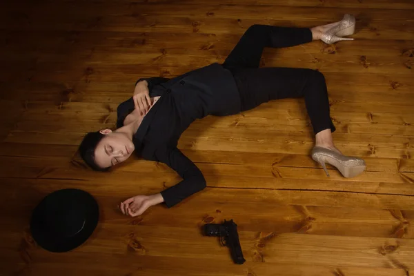 Femme en costume noir avec pistolet couché sur le sol — Photo