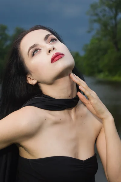 Beautiful brunette woman in black dress and black cloak — Stock Photo, Image