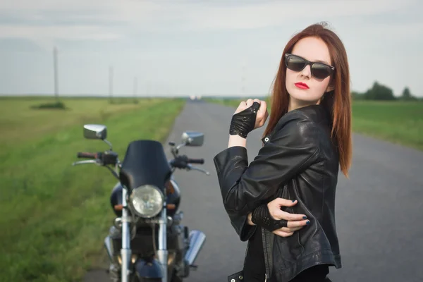 Chica motorista en una chaqueta de cuero posando cerca de la motocicleta — Foto de Stock