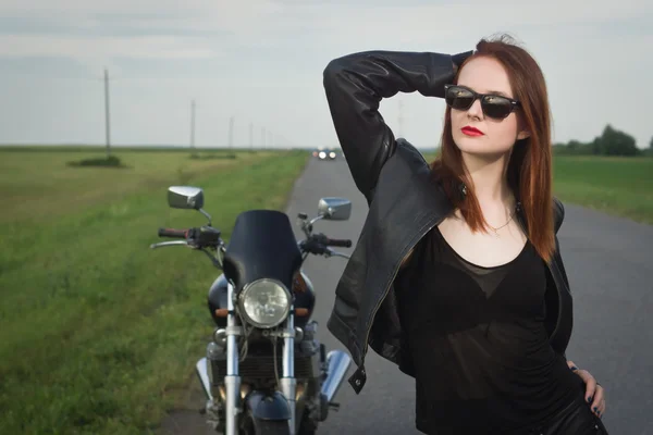 Chica motorista en una chaqueta de cuero posando cerca de la motocicleta — Foto de Stock