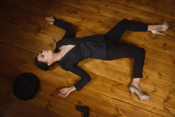 Woman in a black suit with gun lying on the floor Stock Image