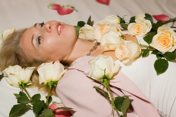Mooie vrouw met rozen liggend op het bed — Stockfoto