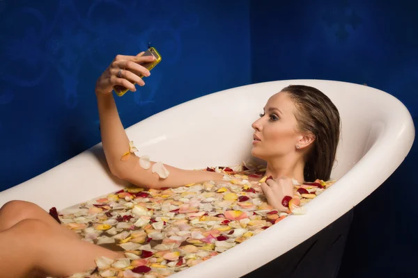 Belle femme sexy dans le bain avec des pétales de fleurs tout en utilisant le — Photo