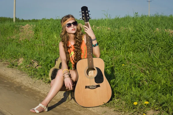 Joven chica hippie sentada en un campo de verano con su guitarra — Foto de Stock