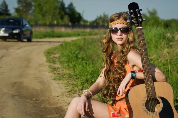 Hippie flicka reser med sin gitarr på en väg — Stockfoto