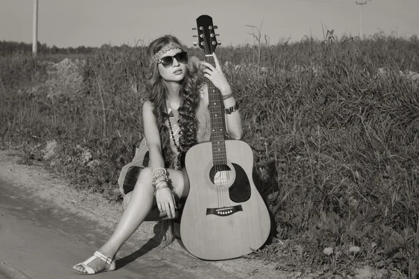 Hippie meisje met haar gitaar rijdend over de weg — Stockfoto