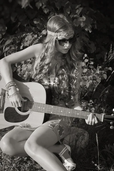 Giovane donna seduta su un campo e suonare la chitarra — Foto Stock