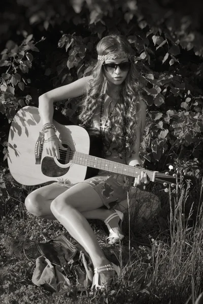 Young woman sitting on a field and playing guitar — Stock Photo, Image