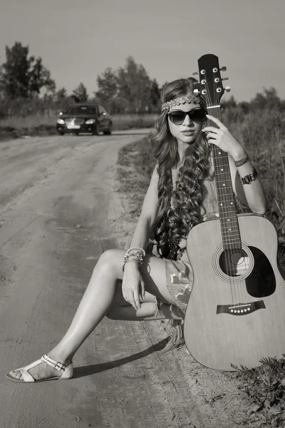 Hippie flicka reser med sin gitarr på en väg — Stockfoto