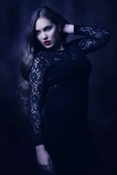 Mooie vrouw in een zwarte jurk in de donkere kamer — Stockfoto