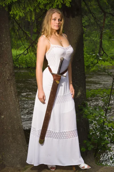 Hermosa mujer en vestido blanco con espada en un bosque salvaje — Foto de Stock